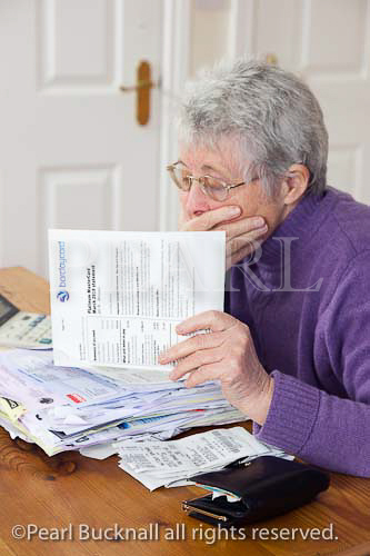 Senior woman pensioner with a big pile of bills with 
hand over her mouth looking shocked at a large 
credit card bill. UK Britain Europe. 