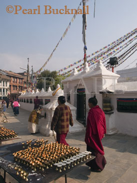 BOUDHANATH STUPA BASE with stalls of burning 
candles to celebrate new moon and Buddhist monks 
walking clockwise past prayer wheels.  Kathmandu 
Nepal Asia
