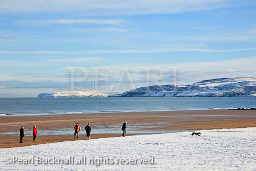 View to the Great Orme across Red Wharf Bay with 
people walking on the snow covered beach in winter
Benllech, Isle of Anglesey, North Wales, UK, Britain. 

Keywords: coast scene snowfall Britain British weather 
Welsh