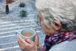 Senior woman holding a warm drink looking out of the 
window on a cold snowy day in winter. UK Britain 
Europe