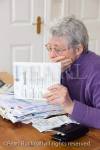 Senior woman pensioner with a big pile of bills with 
hand over her mouth looking shocked at a large 
credit card bill. UK Britain Europe. 