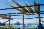 Traditional Inuit kayaks on a rack by coast with icebergs 
from Ilulissat Icefjord floating in sea offshore. Ilulissat 
(Jakobshavn), Qaasuitsup, Greenland