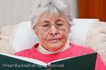 Elderly woman wearing spectacles sat reading a book. 
England, UK, Britain