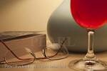 Glass of red wine with lit bedside table lamp 
paperback book and spectacles in the evening

Keywords: light still life home homely concept