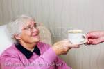 Senior woman looking up and smiling at a carer giving 
her a cup of tea. England, UK, Britain. MR 13/29, MR 
13/30