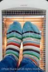 Person wearing colourful striped woolly socks 
warming feet in front of a low energy Halogen room 
heater. England UK Britain