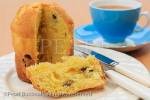 A slice of Panettone Italian Christmas fruit bread 
cake on a plate with a cup of tea on a table top. 
