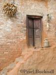 POT URN on TERRACOTTA STEPS to old wooden 
doorway in traditional style building with corn pods 
hanging to dry in rural village near Lalitpur. 
Bungamati, Kathmandu Valley, Nepal, Asia 
