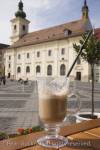 Latte Macchiato with straw in glass on table in street 
cafe in Piata Mare in historic city centre of 
Hermannstadt. Sibiu Transylvania Romania Europe
