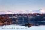 Menai Strait with Menai suspension bridge and 
snow on mountains of Snowdonia in winter. Menai 
Bridge (Porthaethwy), Isle of Anglesey (Ynys 
Mon), North Wales, UK, Britain. 