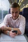 Young man train passenger commuting to work using 
an iPhone to send a text message. England UK Britain 