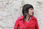 Young woman wearing a red coat standing by a white 
wall with peeling paint. UK Britain Europe. 