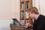 England, UK, Britain, Europe. Young man squinting at 
the screen of a laptop computer on a chair in the living 
room.