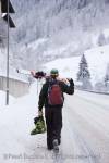 Skier carrying skis and ski boots walking down snow 
covered Alpine road in mid winter. St Anton am 
Arleberg, Tyrol, Austria, Europe