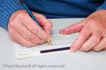 Close-up of a mature woman writing a cheque to pay 
a bill. England, UK, Britain