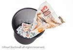 Composite image of a �10 note screwed up and 
being thrown away in a black waste paper bin on 
white from above to illustrate wasting money 
concept