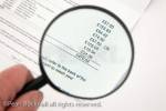 Person holding a magnifying glass to look at a large 
credit card bill. MR 10/21
